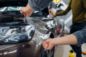 Male worker applies car protection film on front fender. Installation of coating that protects the paint of automobile from scratches. New vehicle in garage, tuning procedure