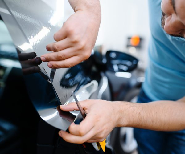 Male wrapper installs car tinting, tuning service. Worker applying vinyl tint on vehicle window in garage, tinted automobile glass